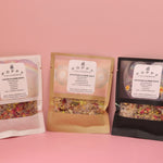 All three of the Poppy California Bath Salt Packets on a pink background.
