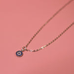 The Sterling Silver Dainty Blue Evil Eye Necklace on a pink background