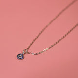 The Sterling Silver Dainty Blue Evil Eye Necklace on a pink background