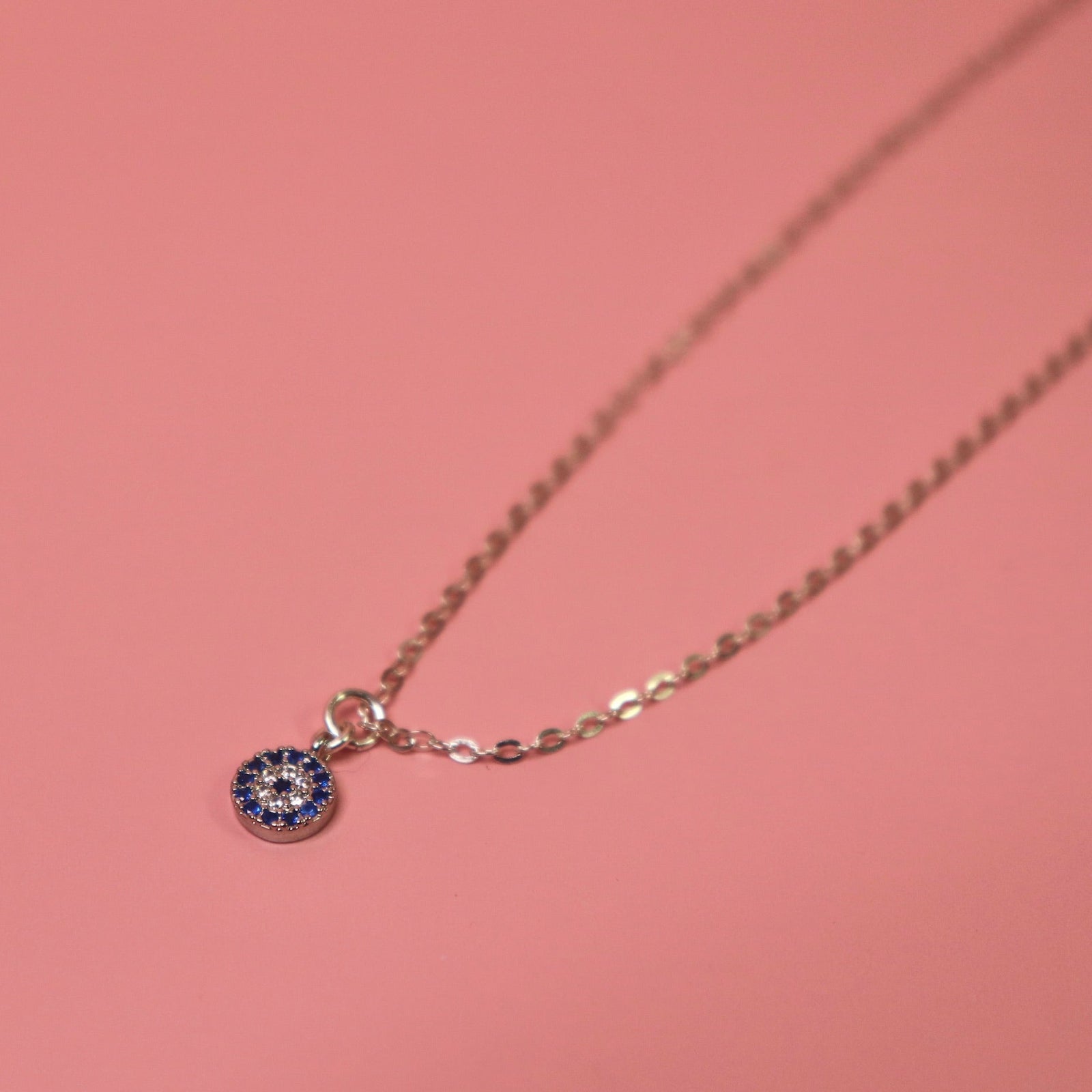 The Sterling Silver Dainty Blue Evil Eye Necklace on a pink background
