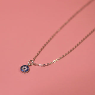 The Sterling Silver Dainty Blue Evil Eye Necklace on a pink background