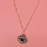 The Sterling Silver Purple Evil Eye Necklace with Paperclip Chain on a pink background.