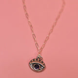 The Sterling Silver Purple Evil Eye Necklace with Paperclip Chain on a pink background.