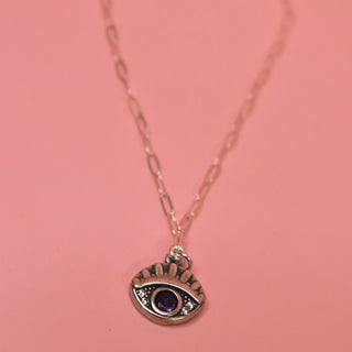 The Sterling Silver Purple Evil Eye Necklace with Paperclip Chain on a pink background.