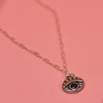 The Sterling Silver Purple Evil Eye Necklace with Paperclip Chain on a pink background.