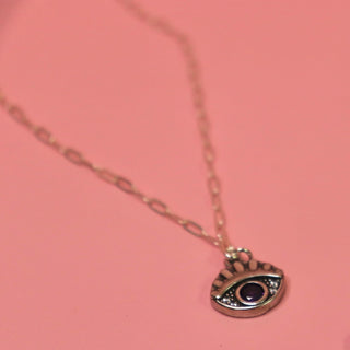 The Sterling Silver Purple Evil Eye Necklace with Paperclip Chain on a pink background.