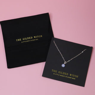The Sterling Silver Dainty Blue Evil Eye Necklace on a pink background