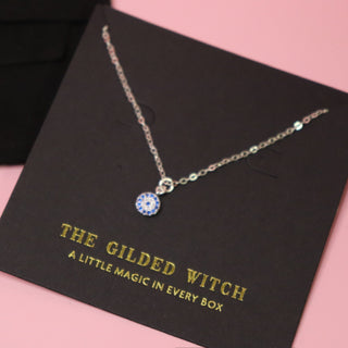 The Sterling Silver Dainty Blue Evil Eye Necklace on a pink background