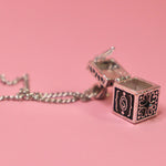 The Vintage Silver Box Locket Necklace on a pink background with its locket open.