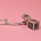 The Vintage Silver Box Locket Necklace on a pink background with its locket open.