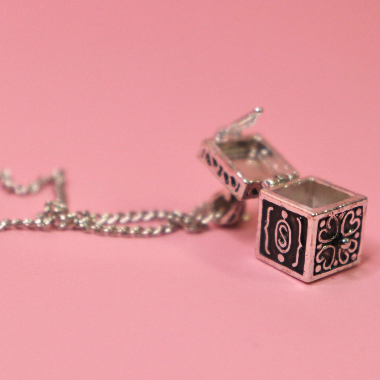 The Vintage Silver Box Locket Necklace on a pink background with its locket open.