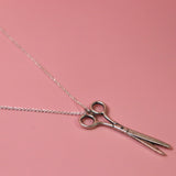 An up-close image of the Vintage Silver Scissors Charm Necklace on a pink background.