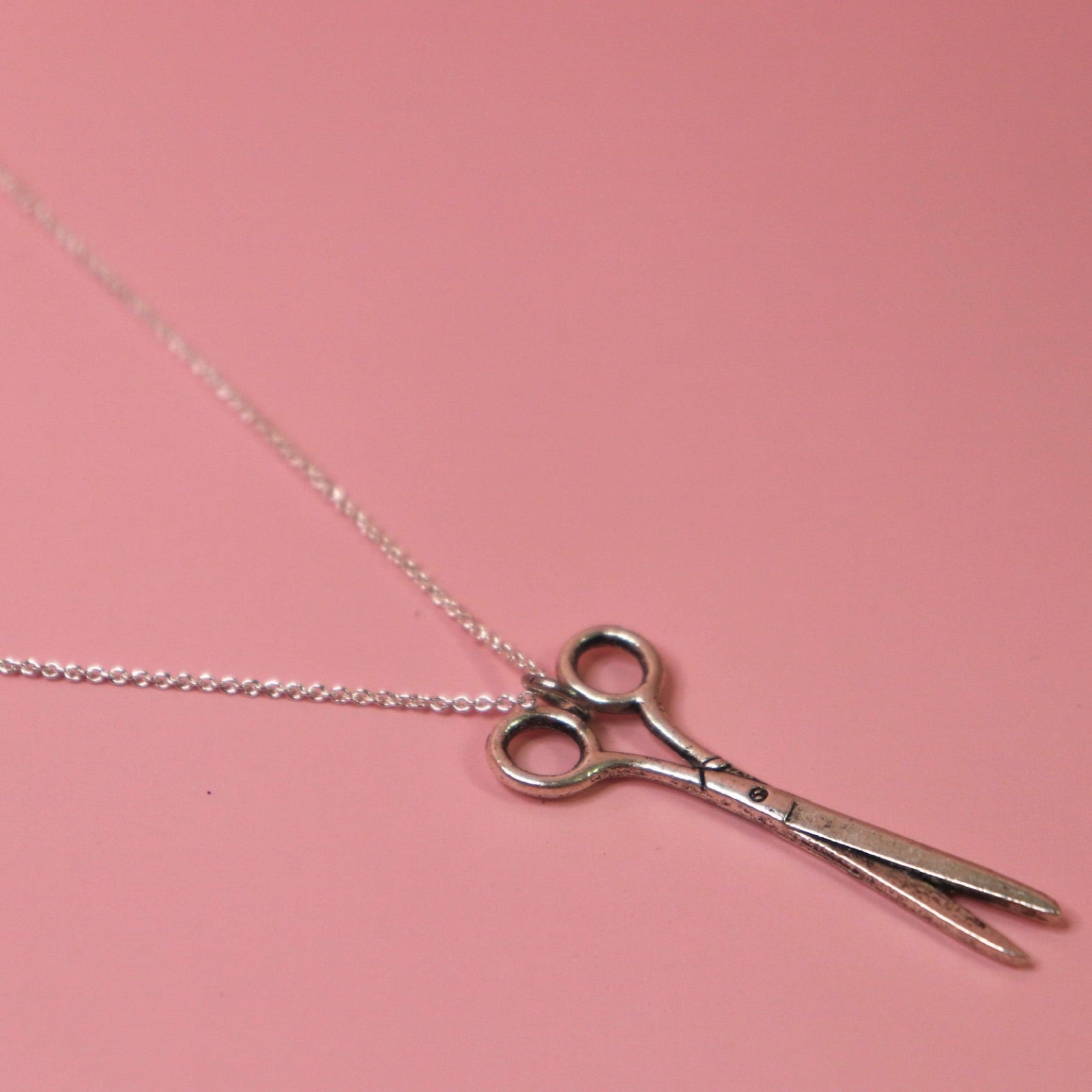 An up-close image of the Vintage Silver Scissors Charm Necklace on a pink background.