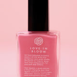 The Love in Bloom Nail Polish with Micronized Rose Quartz & Pink Calcite on a pink background.