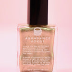 The Abundance Boost Nail Polish with Micronized Pyrite on a pink background.