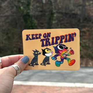 Someone holding the Keep On Trippin 4 Inch Sticker in front of a road.