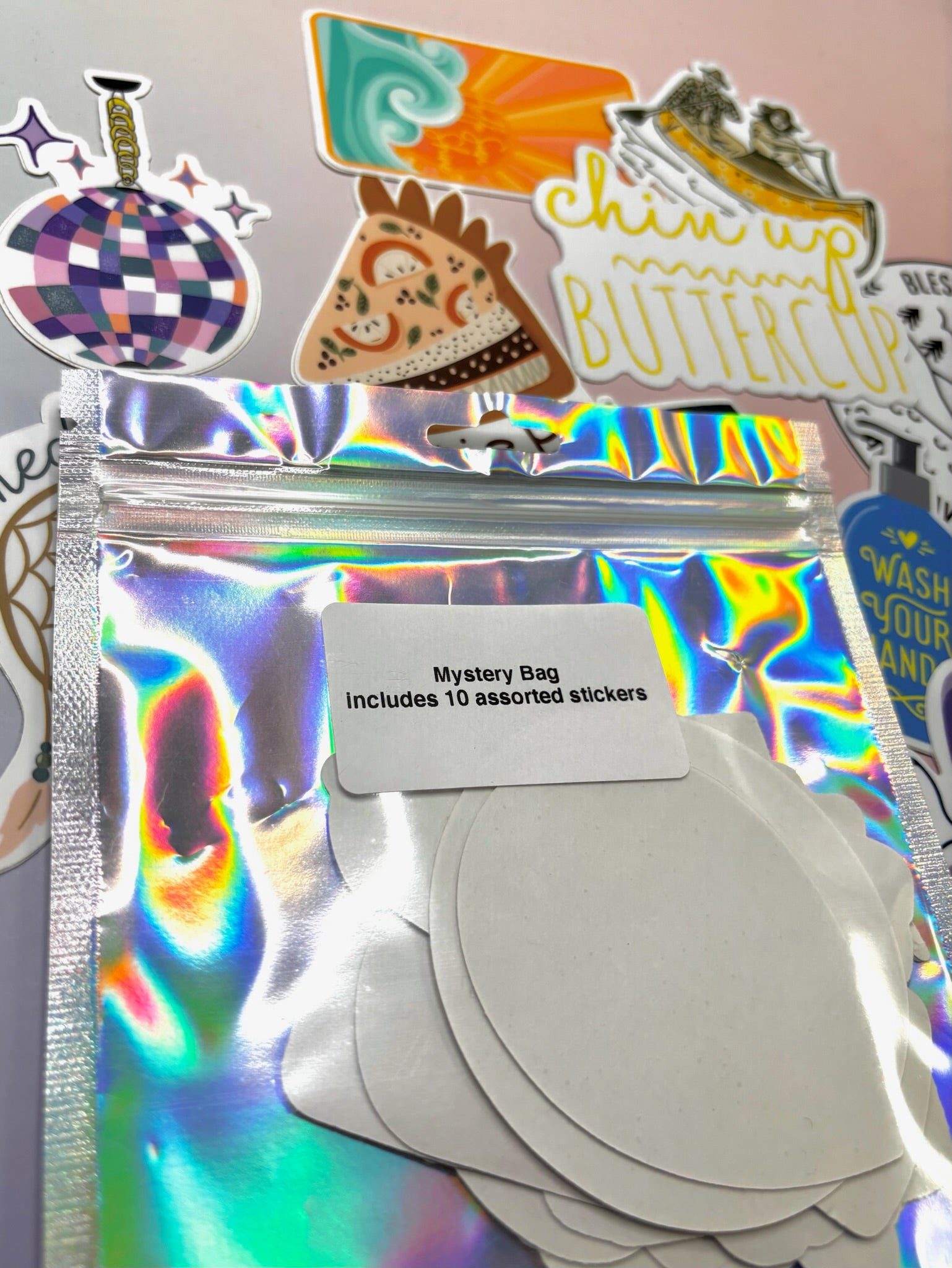 The back of the Fun Mystery Sticker Bag on a pink background with stickers surrounding it.