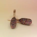Two of the '7 Chakras' Palo Santo Pops - 3"-4" Smudge Sticks on a pink and yellow background.