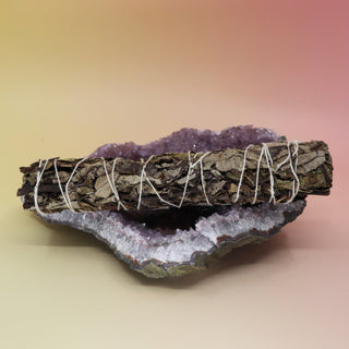 The Black Sage Smudge Stick 9 in. on an amethyst piece all on a pink and yellow background.