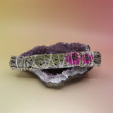 The Dahlia White Sage Smudge Stick 9 in. on an amethyst piece all on a pink and yellow background.