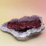 The Organic Dragon's Blood Sage - 6 in. Banishing, Protection, and Sexuality Smudge Stick on an amethyst piece all on a pink and yellow background.