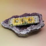 The Organic Sunflower White Sage  - 4 in. Smudge Stick on an amethyst piece all on a pink and yellow background.