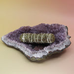 The Organic Protection Ruda Rue Sage 4 in. Smudge Stick on an amethyst piece all on a pink and yellow background.