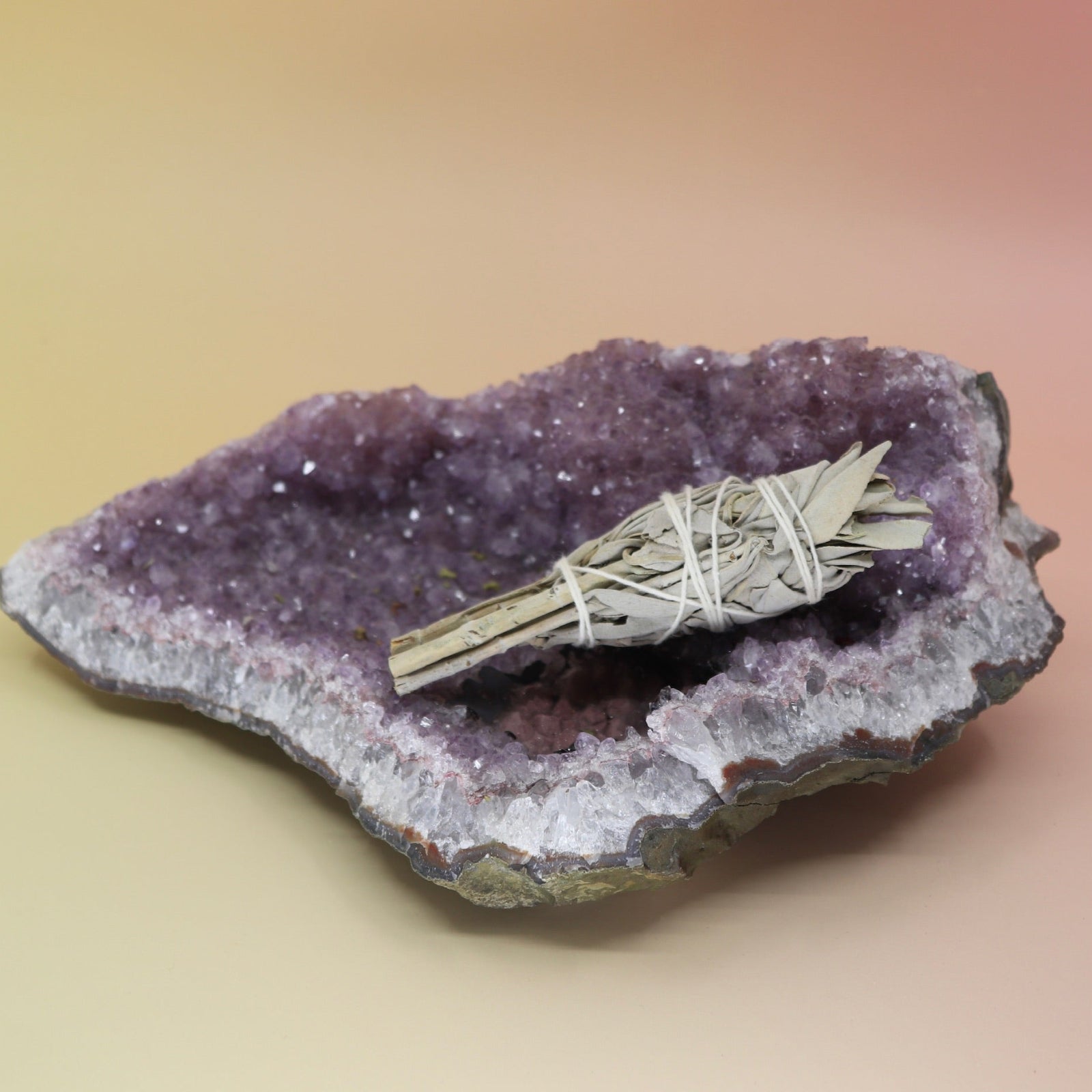 The California White Sage Torch 4 in. on an amethyst piece on a pink and yellow background.