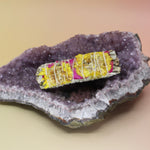 The 'Amor' Organic White Sage with Rose Petals and Sunflowers - 4 in. Sage Smudge Stick on an amethyst piece all on a pink and yellow background.