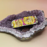 The 'Amor' Organic White Sage with Rose Petals and Sunflowers - 4 in. Sage Smudge Stick on an amethyst piece all on a pink and yellow background.