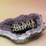 The 'Terra' Organic Black Colored White Sage with Cream Leaves - 4 in. Smudge Stick on an amethyst piece all on a pink and yellow background.