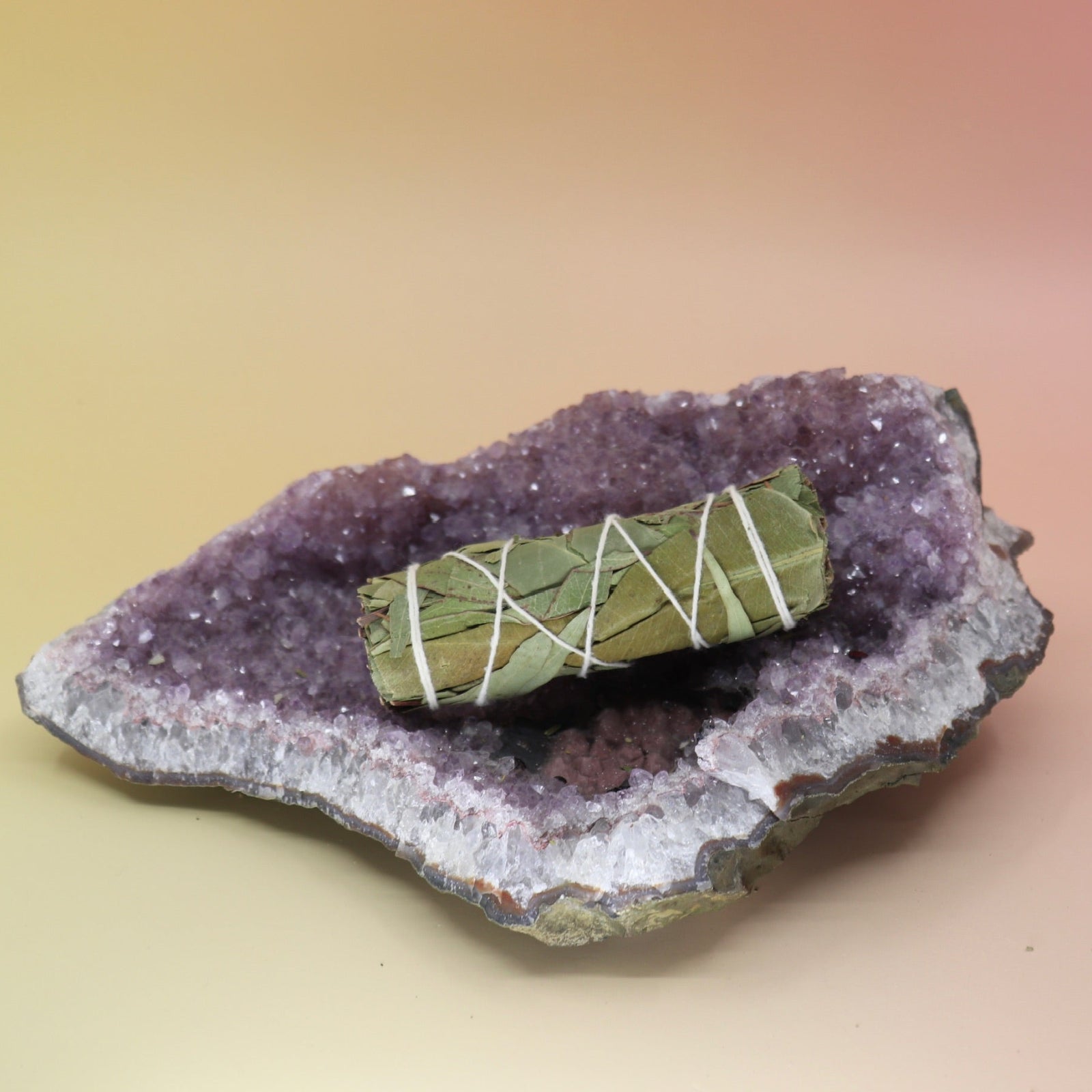 The Eucalyptus Sage Smudge Stick 4 in. on an amethyst piece on a pink and yellow background.