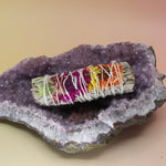 The 'Joy' Floral White Sage - 4 in. Smudge Stick on an amethyst piece all on a pink and yellow background.