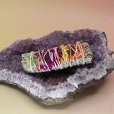 The 'Joy' Floral White Sage - 4 in. Smudge Stick on an amethyst piece all on a pink and yellow background.