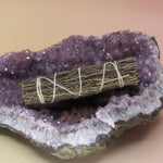 The Organic Copal Sage 4 in. Smudge Stick on an amethyst piece all on a pink and yellow background.