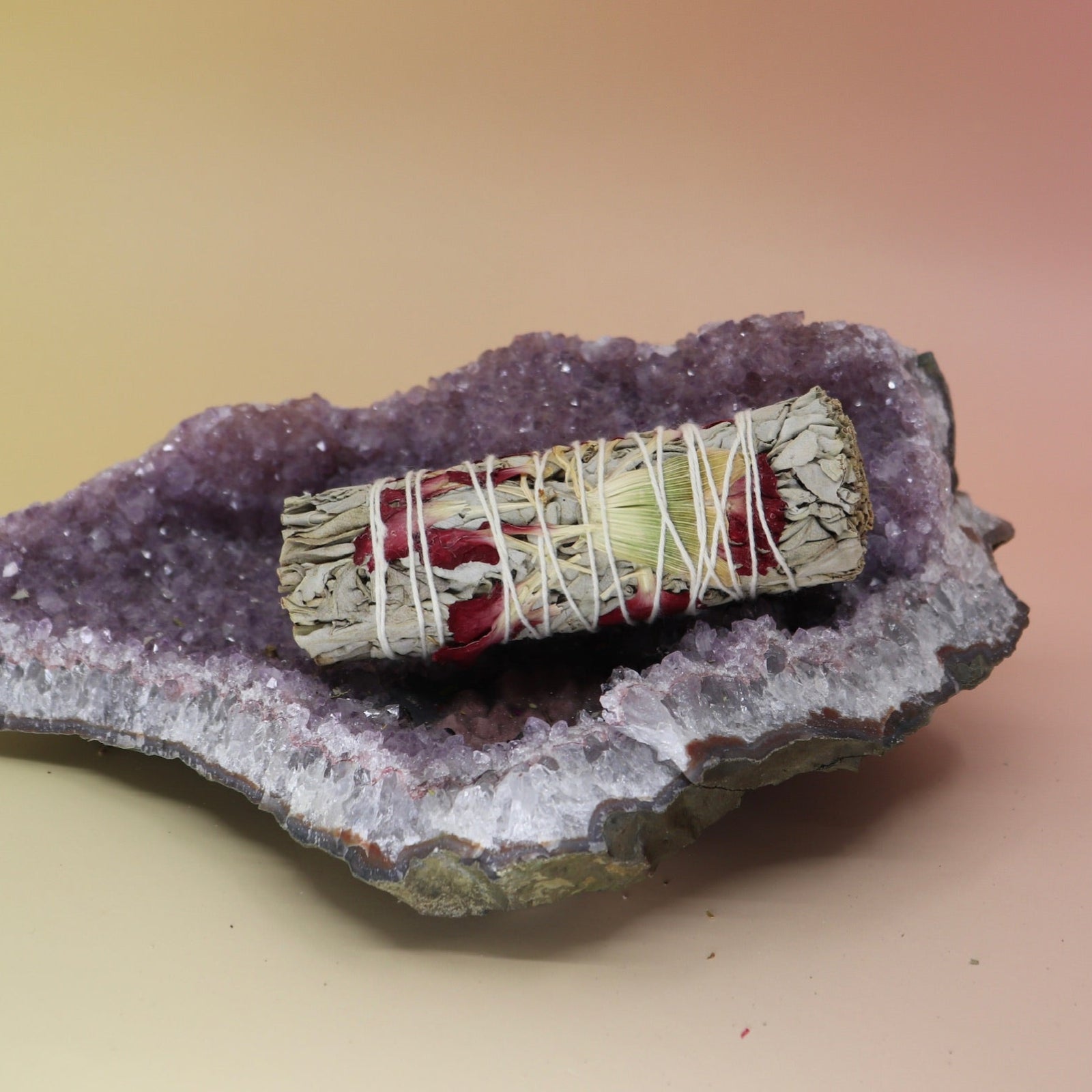 The 'Spring Morning' - Organic Floral White Sage with Daisy Flowers - 4 in. Smudge Stick on an amethyst piece on a pink and yellow background.