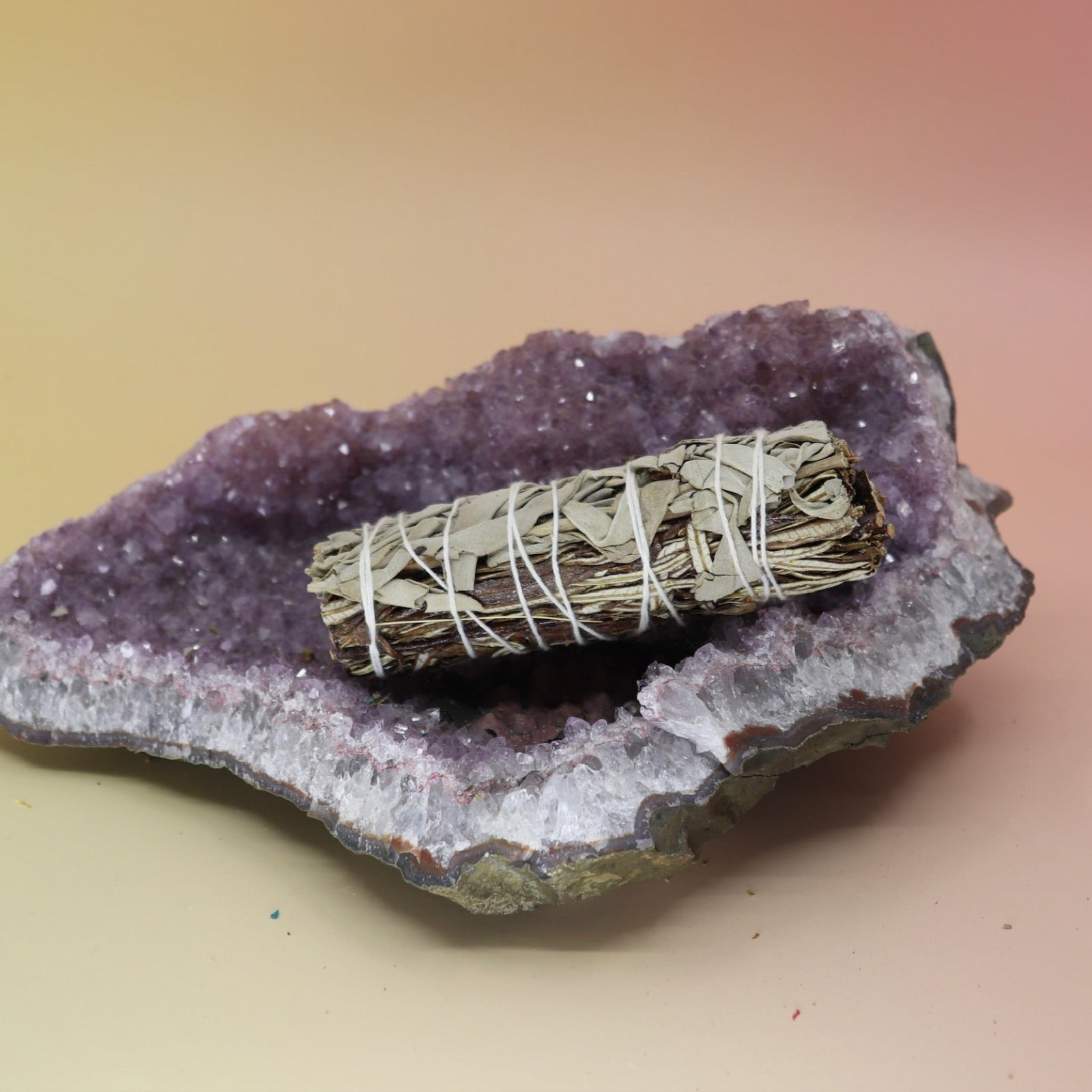 The Organic White Sage & Yerba Santa - 4 in. Smudge Stick on an amethyst piece on a pink and yellow background.