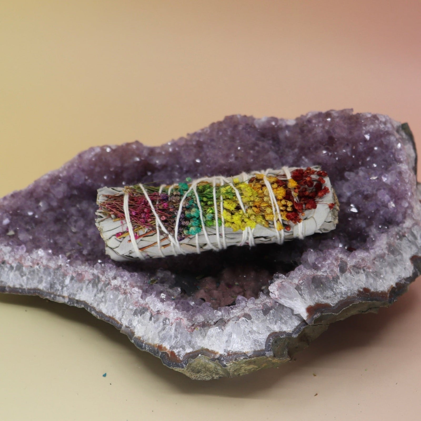 The 'Energy Wheel' Floral White Sage Smudge Stick 4 in. on an amethyst piece on a pink and yellow background.l