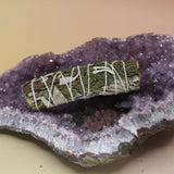 The Organic White Sage & Cedar - 4 in. Purifying and Balancing Smudge Stick on an amethyst piece all on a pink and yellow background.