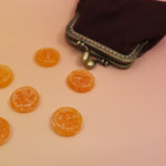 The Pippi Longstocking Gold Coins lying on a yellow surface coming out of a brown coin pouch.
