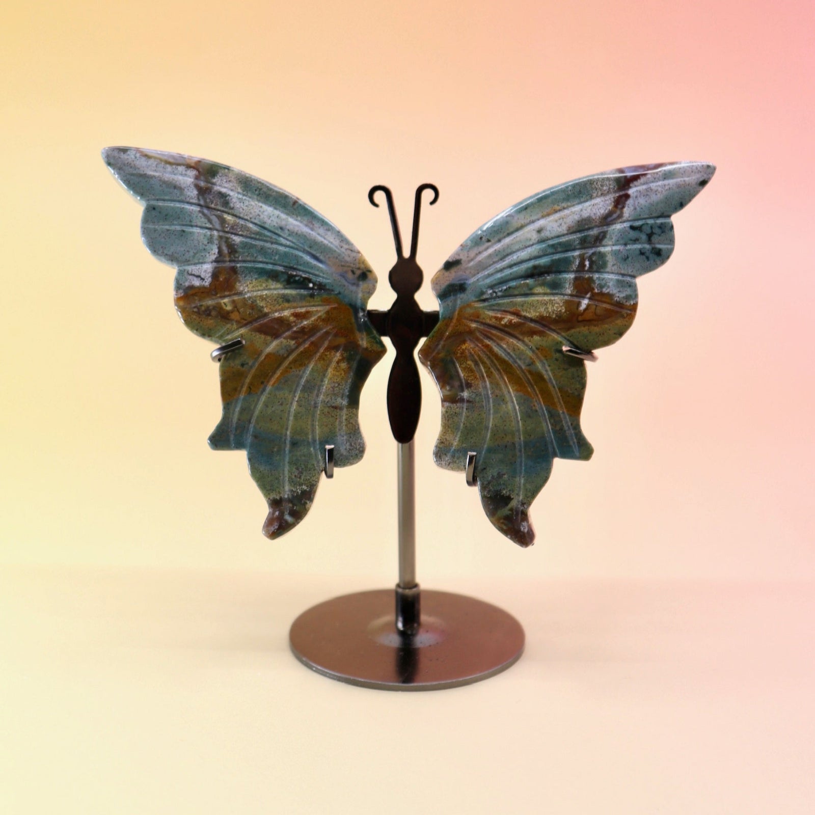 The Natural Marine Jasper Butterfly Crystal with Stand on a pink and yellow background.