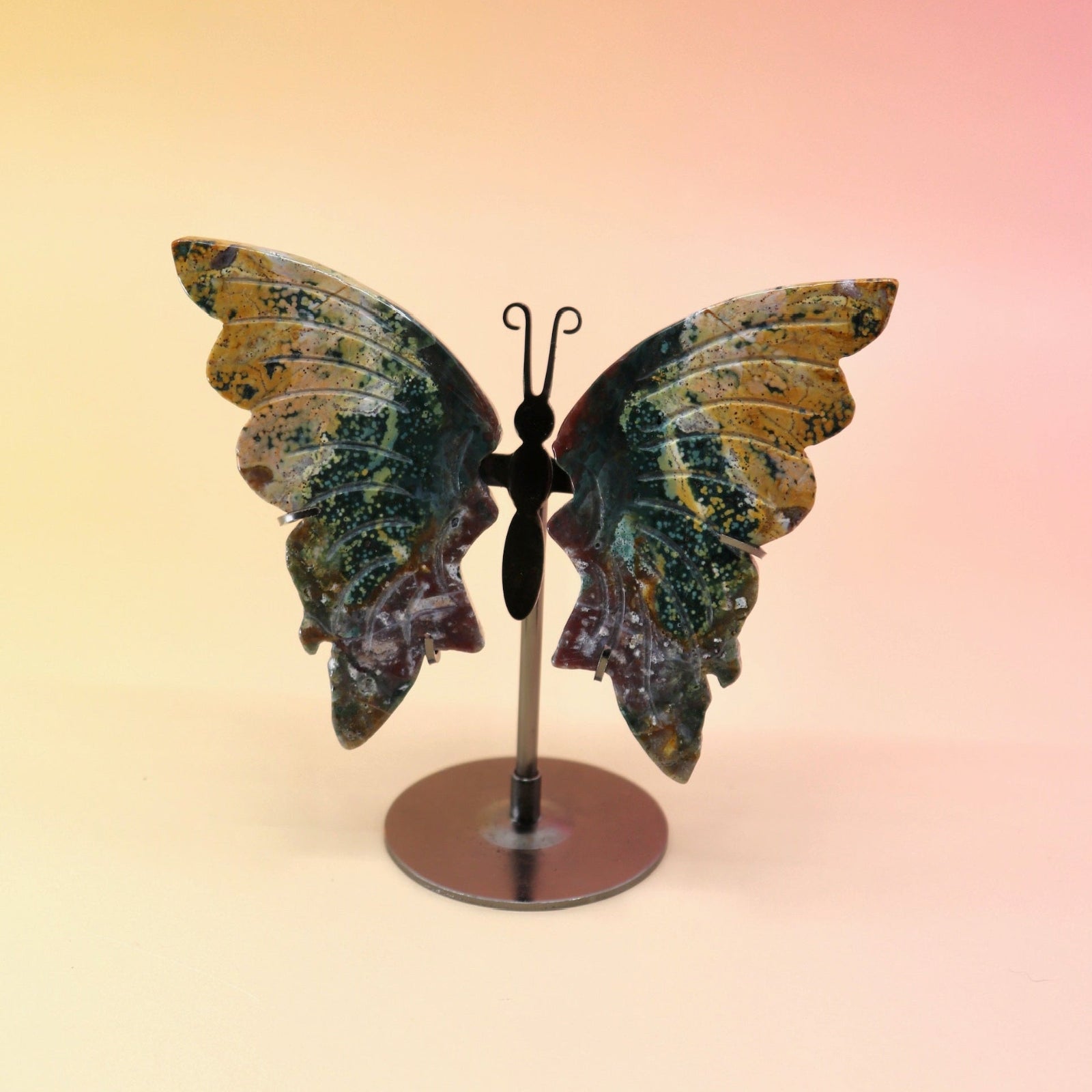 The Natural Marine Jasper Butterfly Crystal with Stand on a pink and yellow background.
