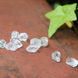Multiple Herkimer Diamond Stones on a rusty red surface with ivy around it.
