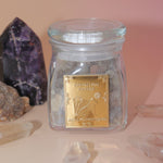 The Royal Frankincense in front of two crystal pieces with crystal points surrounding the jar all on a pink and yellow background.