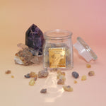 The Royal Frankincense jar with its lid off, in front of two crystal pieces with frankincense surrounding the jar all on a pink and yellow background.