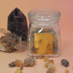 The Royal Frankincense in front of two crystal pieces with frankincense surrounding the jar all on a pink and yellow background.