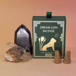 The Mayan Copal + Desert Sage Incense Cone box next to two crystal pieces with two of its incense cones in front of the box all on a pink and yellow backgrounds.