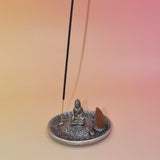 The Silver Buddha Cone and Stick Incense Holder on a pink and yellow background an incense cone and an incense stick on it.