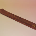 The Om Wooden Incense Burner on a pink and yellow background.