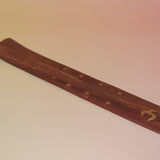 The Om Wooden Incense Burner on a pink and yellow background.